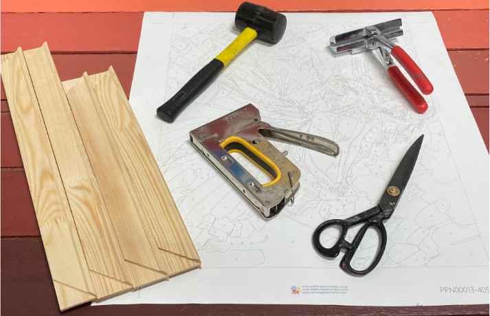 A disassembled wooden frame, a mallet, staple gun, scissors, canvas pliers, and a canvas